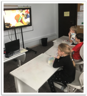 A group of children sitting at a table watching a television

Description automatically generated with low confidence